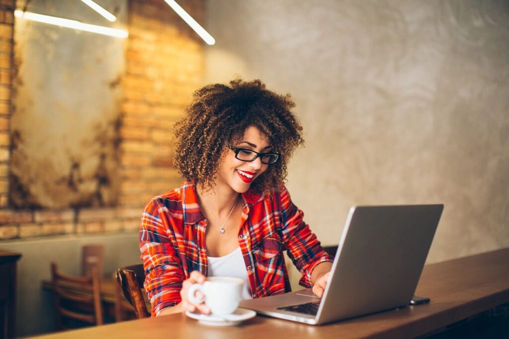 Woman with curly hair working on laptop and drinking coffee